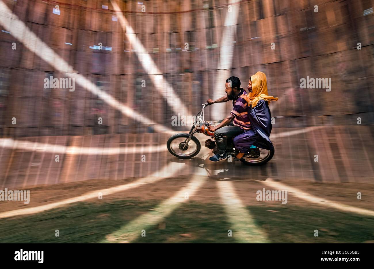 Bogura, Bangladesch - 18. April 2022: Blick auf einen aufregenden Motorradstunt in einem kreisförmigen, hölzernen „Totenbrunnen“, in dem Fahrer und Beifahrer sich gegen g Stockfoto