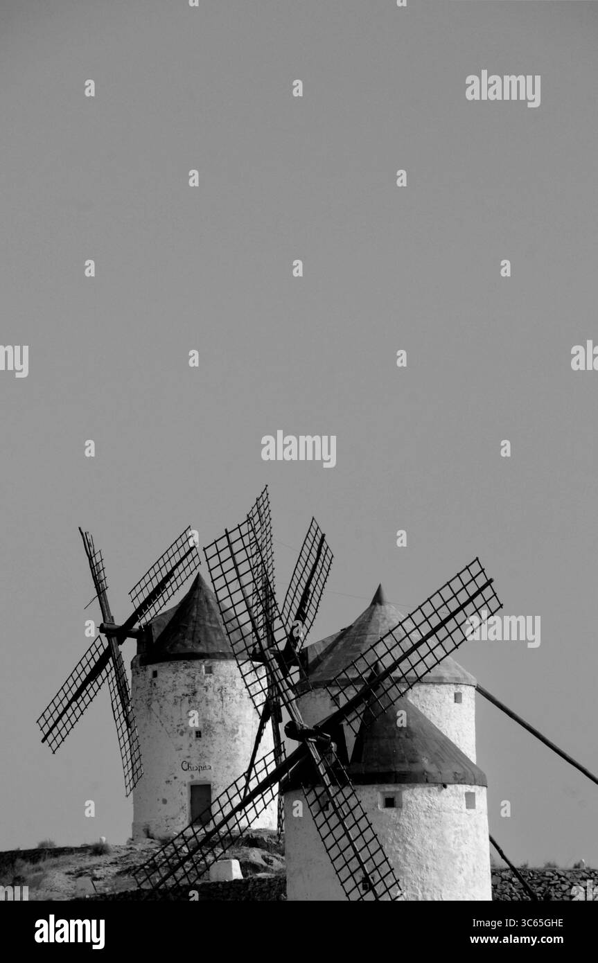 Schwarzweißbild von drei traditionellen Windmühlen, die auf einem Kamm unter klarem Himmel ausgerichtet sind. Die klassischen Gebäude stehen hoch und erinnern an zeitloses ländliches c Stockfoto