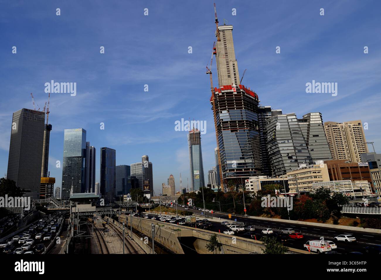 Blick auf ein Hochhaus in Tel Aviv-Jaffa mit auftauchenden Stahl- und Glaskonstruktionen vor klarem Himmel und bewegendem Stadtverkehr. Stockfoto