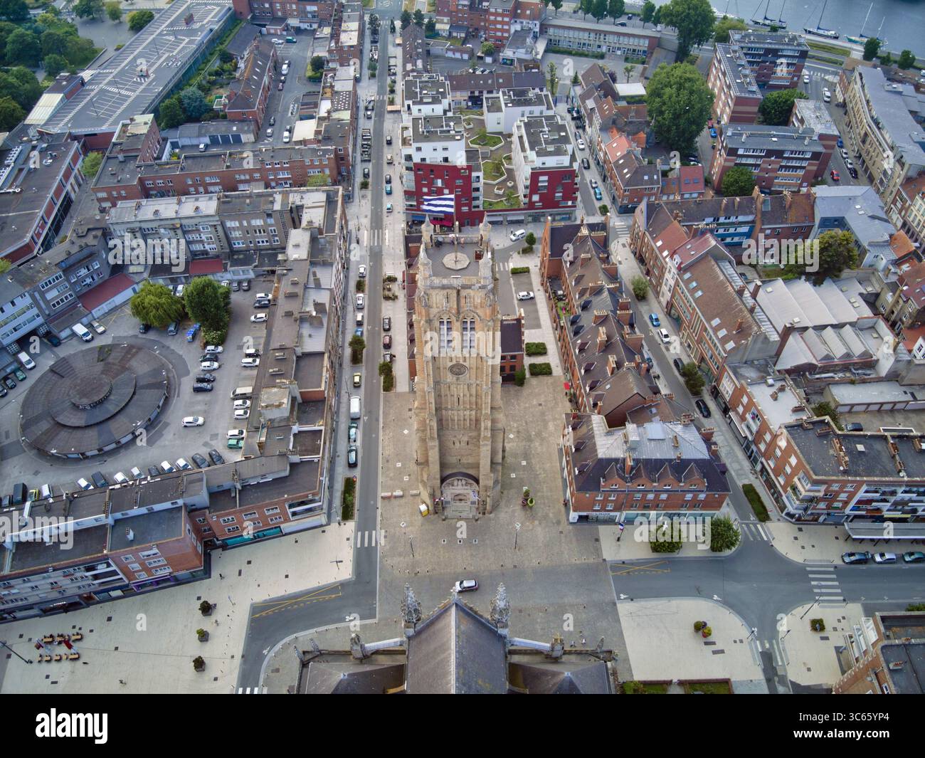 Die hoch aufragende Kirche Saint-Eloi wirft einen langen Schatten über den Place Charles Valentin, eine pulsierende Szene des städtischen Lebens in Dünkirchen, Frankreich. Stockfoto