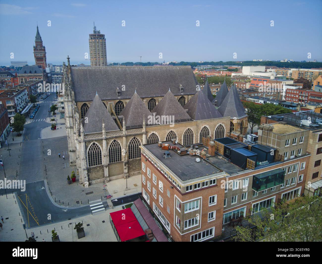 Blick aus der Vogelperspektive auf die große Kirche Saint-Eloi, die einen langen Schatten wirft, ihre gotische Architektur ein Zeugnis der Zeit, inmitten der städtischen Wandteppiche, Dunkirk, Frankreich. Stockfoto