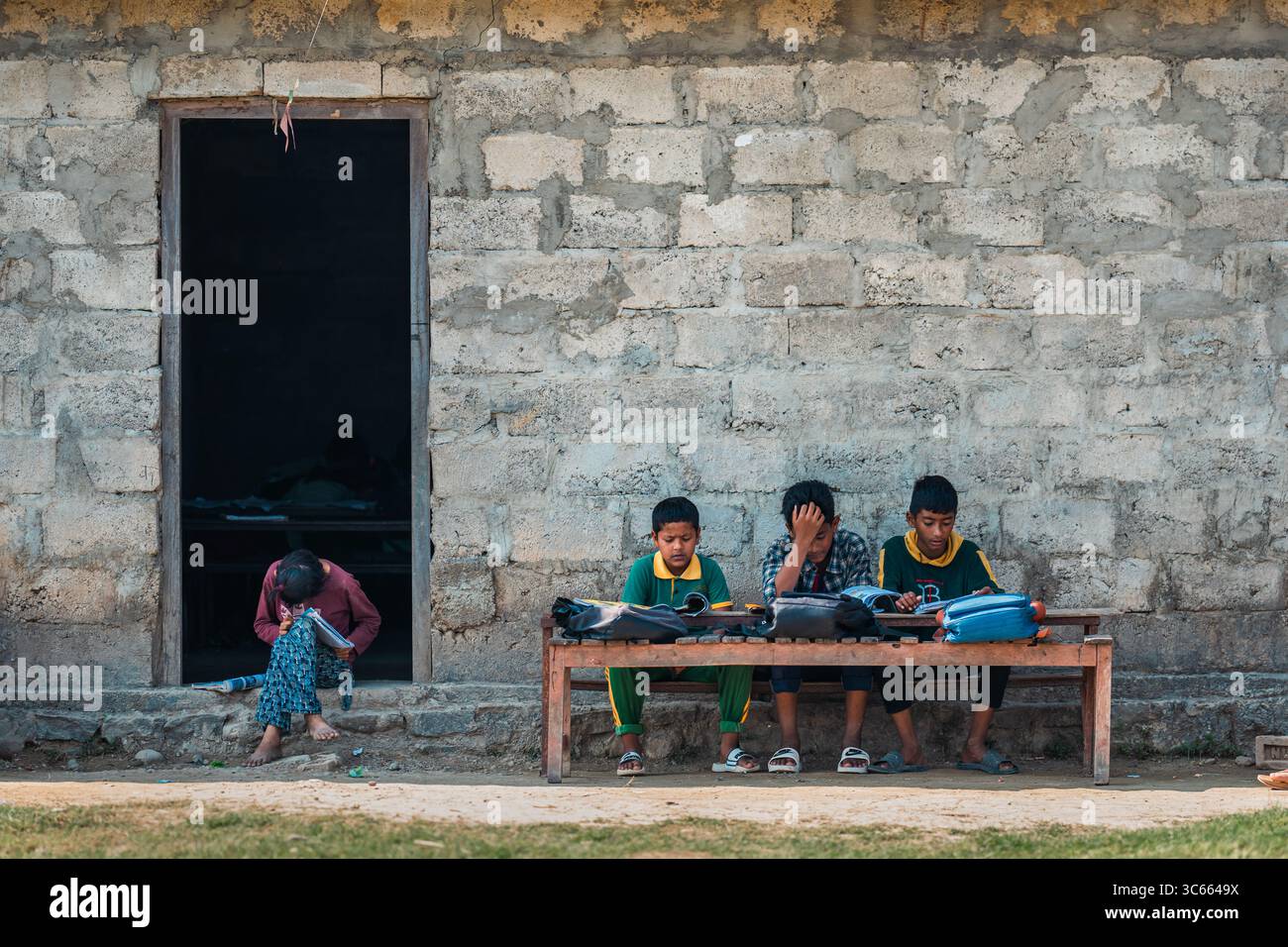 Dhangadhi, Nepal - 03. Mai 2023: Blick auf Kinder, die außerhalb eines robusten, grauen Blockhauses studieren, ihre helle Kleidung ein starker Kontrast zu den gedämpften Tönen. Stockfoto