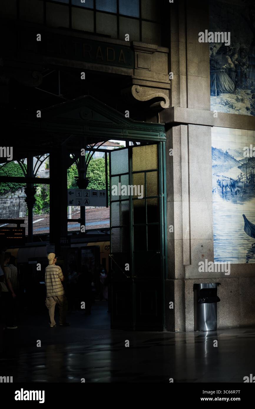 Porto, Portugal - 17. Juni 2022: Blick auf die große Halle des Bahnhofs São Bento, wo Licht durch den Eingang strömt und die Azulejo-Fliesen und die Einzelfigur darunter beleuchtet. Stockfoto