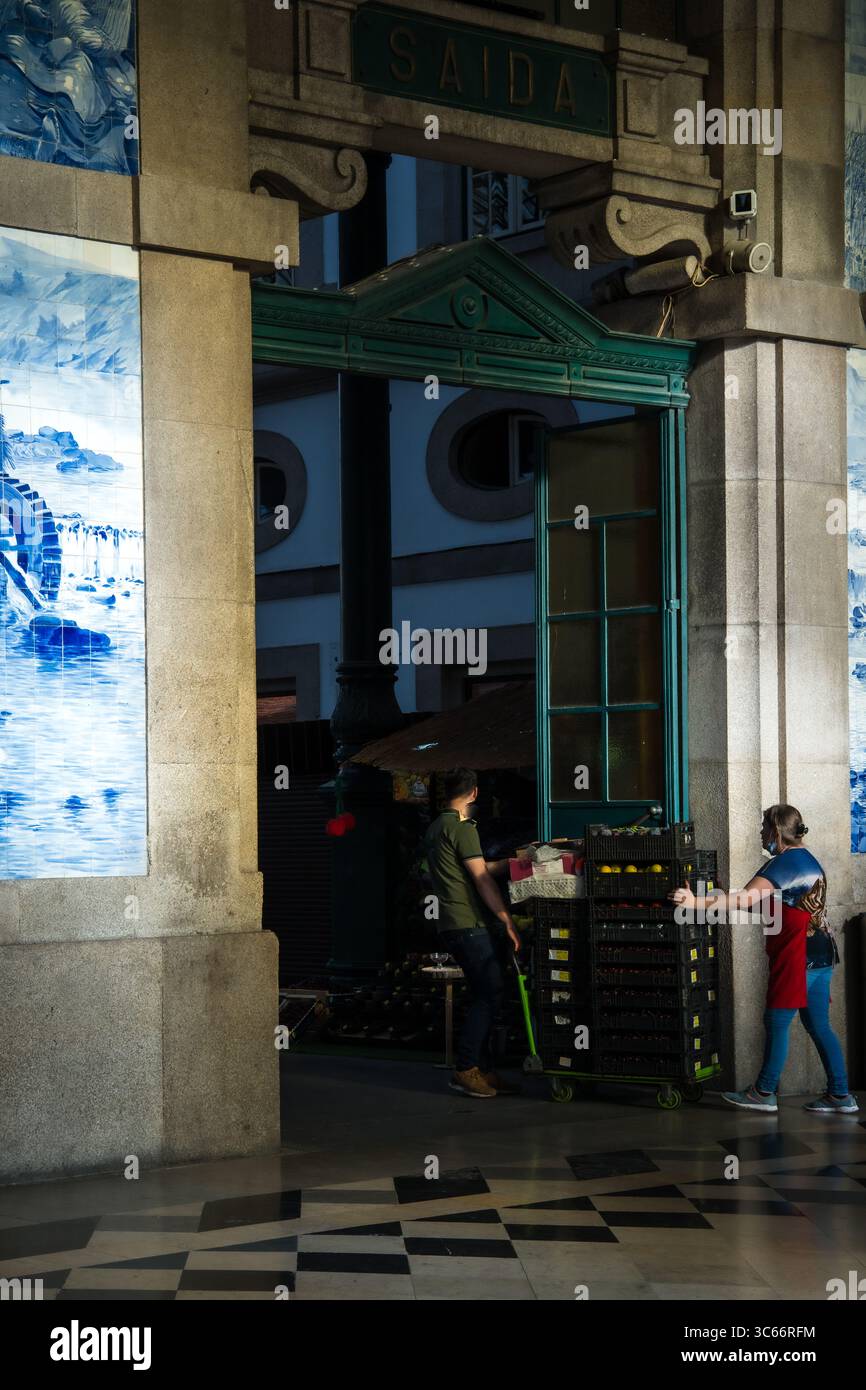 Porto, Portugal - 17. Juni 2022: Blick auf einen Arbeiter, der einen Wagen durch den Eingang des Bahnhofs São Bento schiebt, eingerahmt von Azulejo-Fliesen und kunstvoller Architektur. Stockfoto