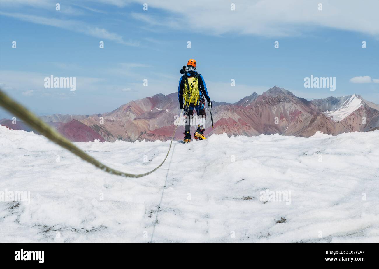 Rückansicht des Seilteams Climber in Bergsteigerausrüstung auf dem Gletscher während des Lenin Gipfels unter klarem Himmel mit Berggipfeln im Hintergrund. Extrem A Stockfoto