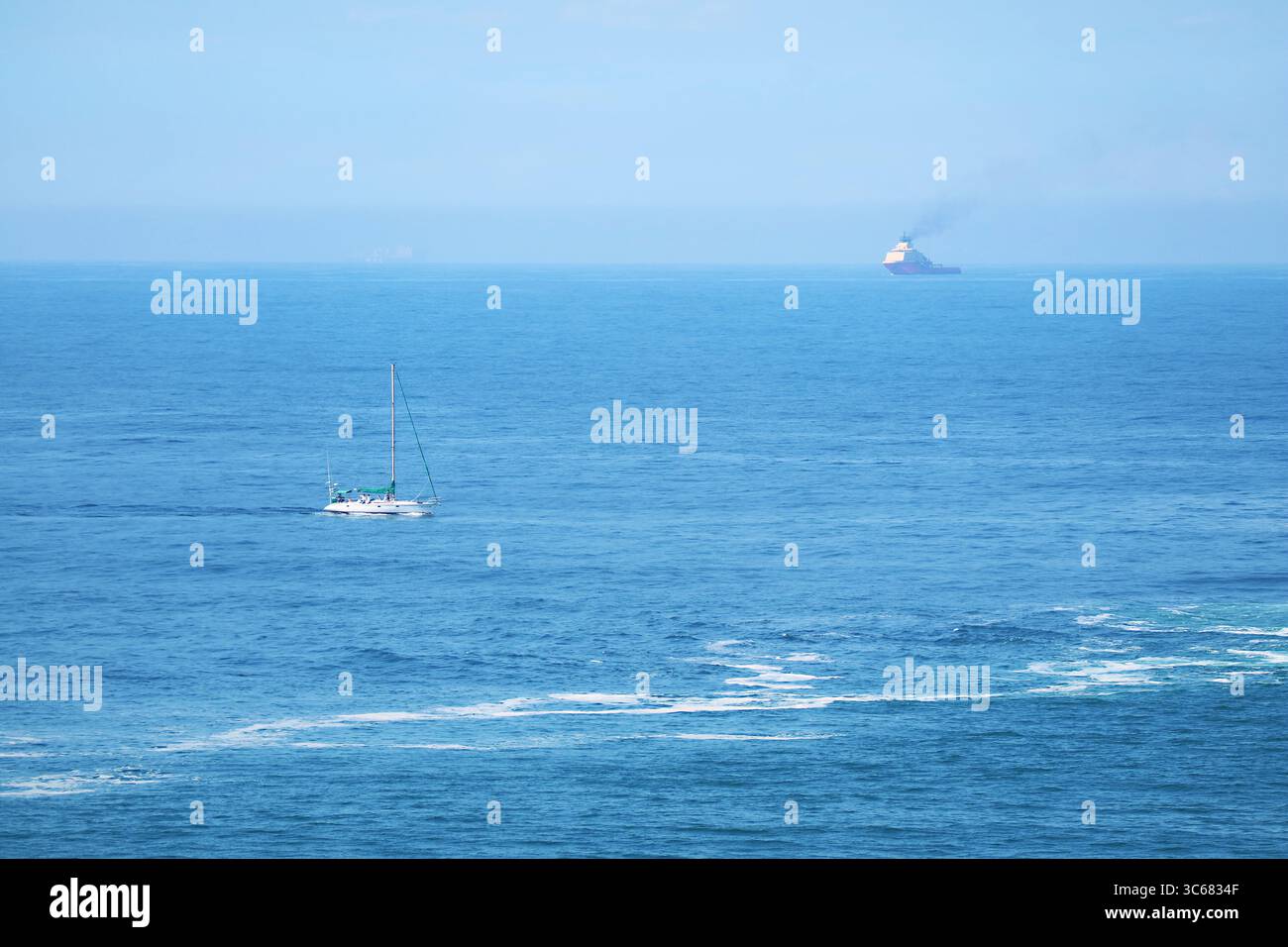 Beeindruckender blauer Atlantik mit einer weißen Yacht und einem Frachtschiff in der Ferne Stockfoto