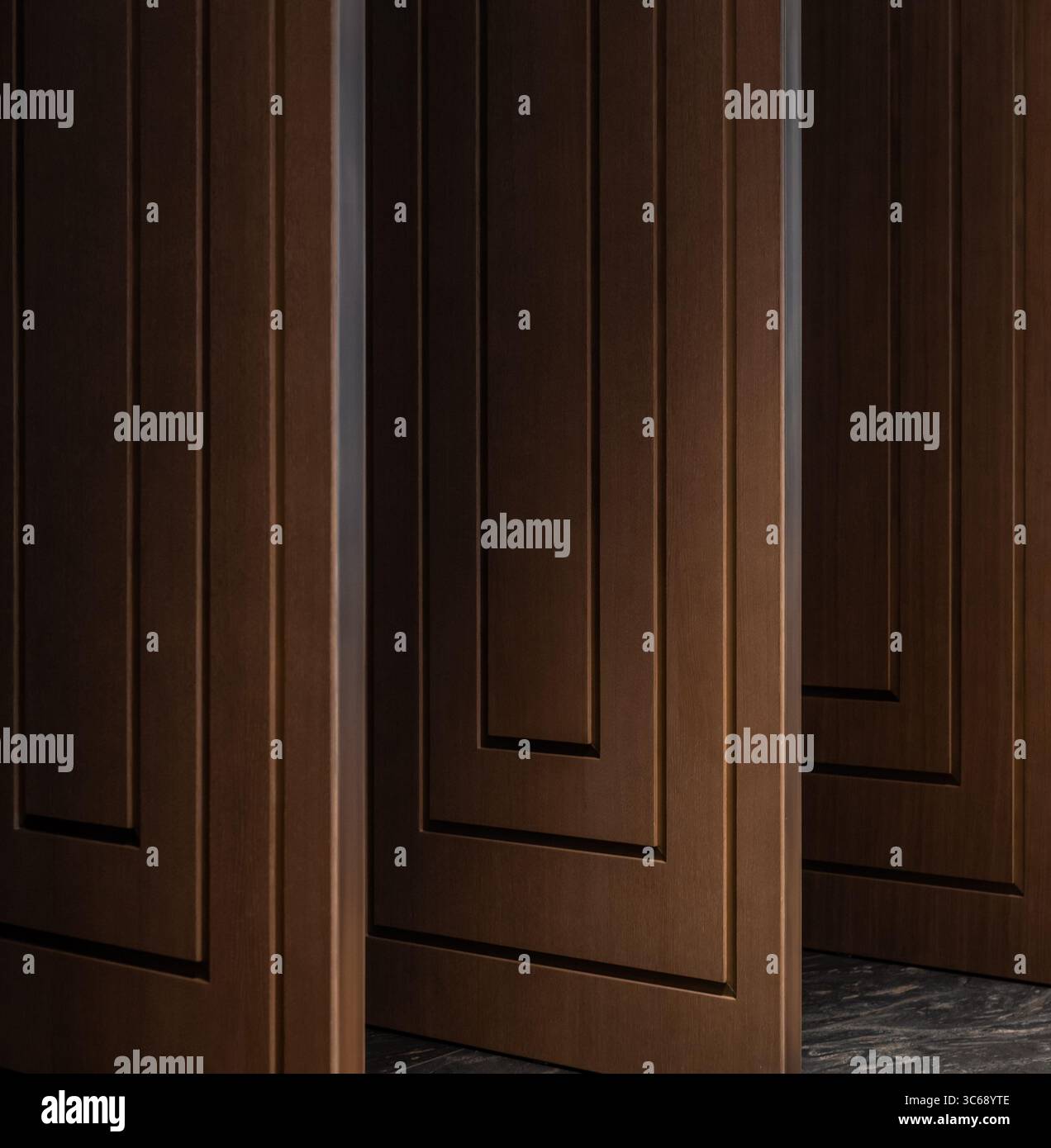 Eine Reihe brauner Holztüren in einem dunklen Raum. Drei offene braune Türen mit rechteckigem Muster. Stockfoto