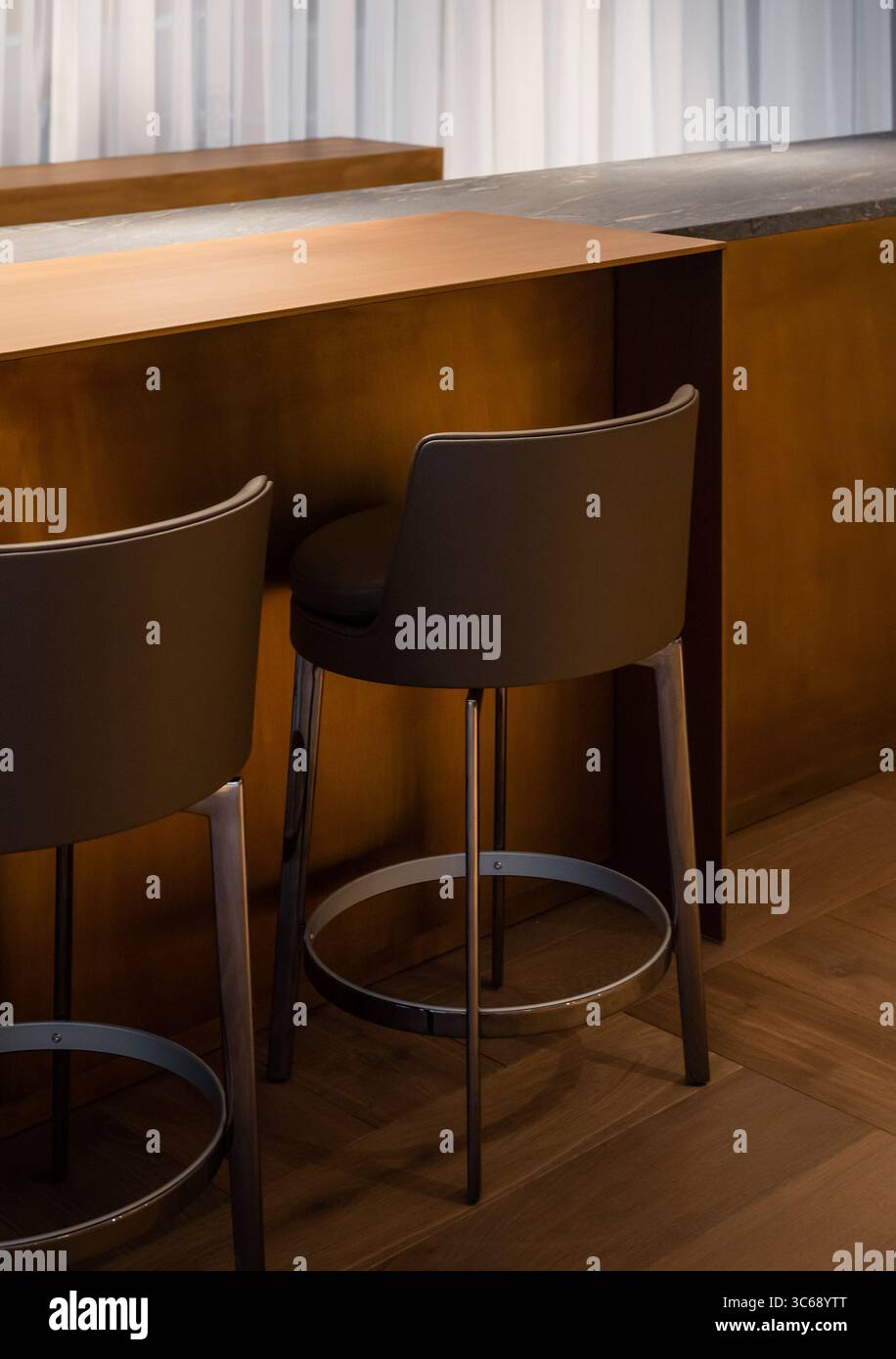 Ein paar Barhocker in der Nähe eines hohen Messingbronzefarbenen Tisches. Leere Hochstühle in der Lobby Lounge Bar mit warmer Beleuchtung. Stockfoto