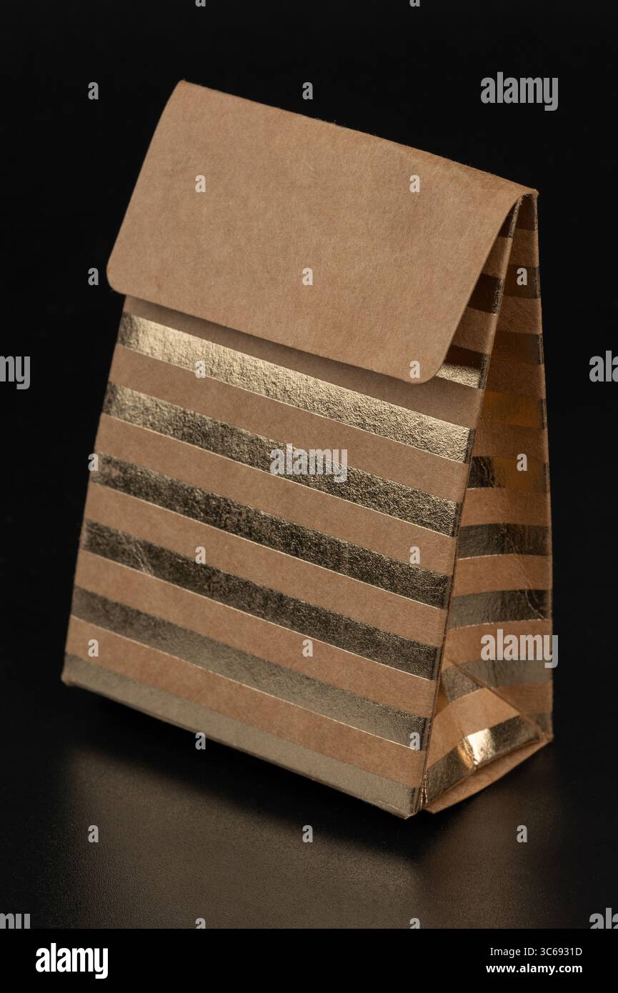 Stilvolle Papiertüte mit goldenen Streifen auf einer schwarzen Oberfläche, die ein modernes Verpackungsdesign veranschaulicht, ideal für Geschenke, Einzelhandel und persönliche Zwecke Stockfoto