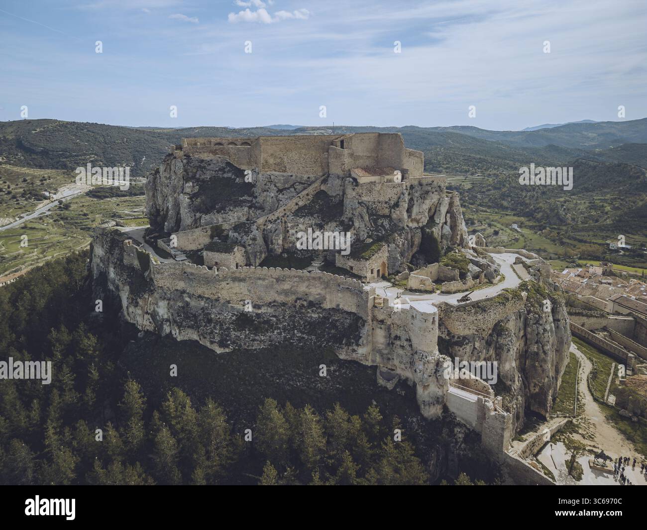 Blick aus der Vogelperspektive auf die imposante Burgfestung, die auf einem felsigen Felsen thront, deren alte Steinmauern sich von den grünen Hügeln, Morella, Valencianisch abheben Stockfoto
