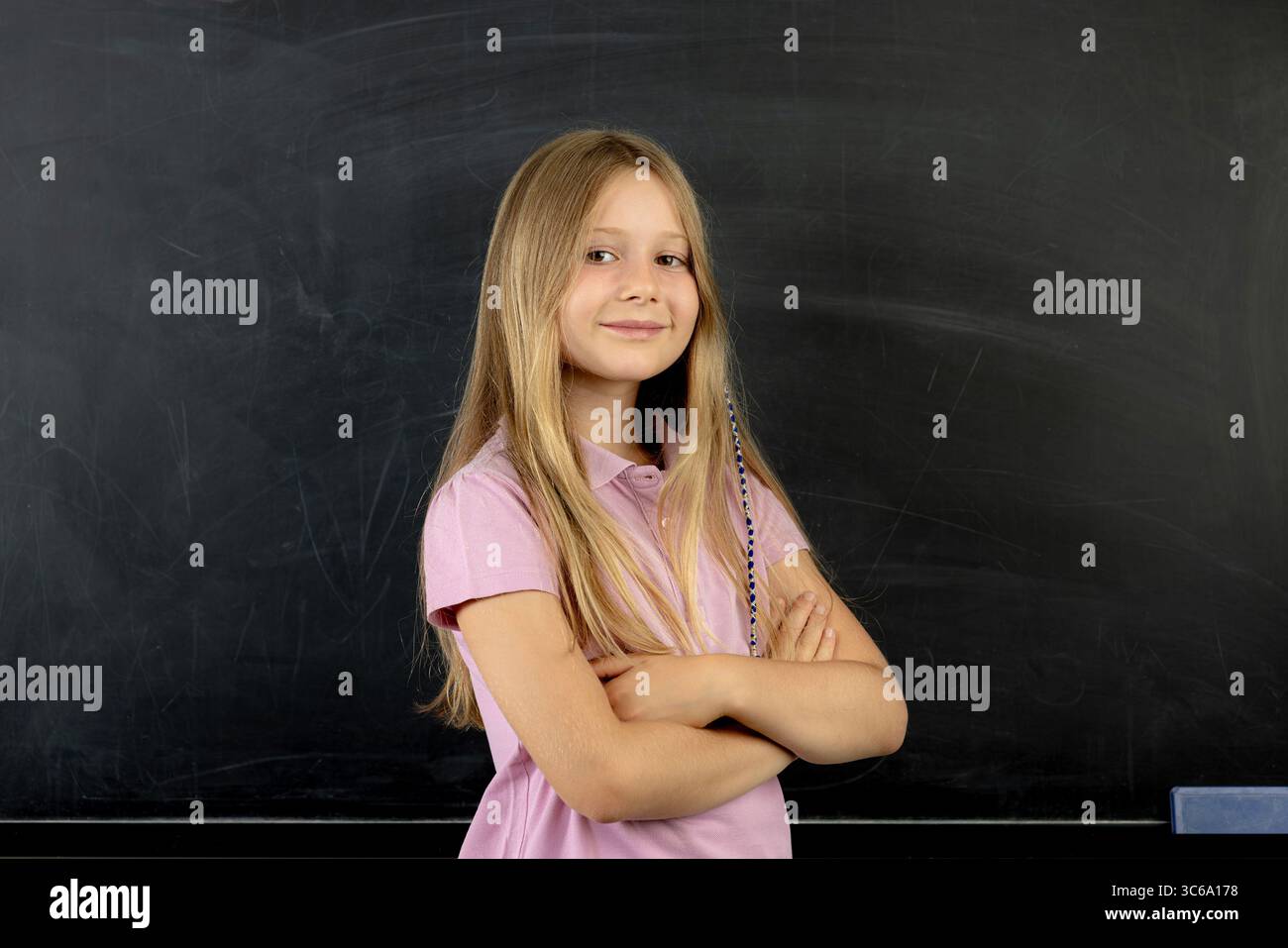 Selbstbewusstes Schulmädchen, das mit gefalteten Armen lächelt Stockfoto