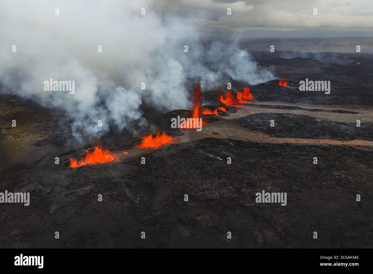 Aus der Vogelperspektive sehen Sie feurige Flüsse aus geschmolzener Lava, die sich durch die dunkle, rauchige Landschaft unter einem rauchigen Himmel schlängeln, Grindavik, Region der südlichen Halbinsel, Island. Stockfoto