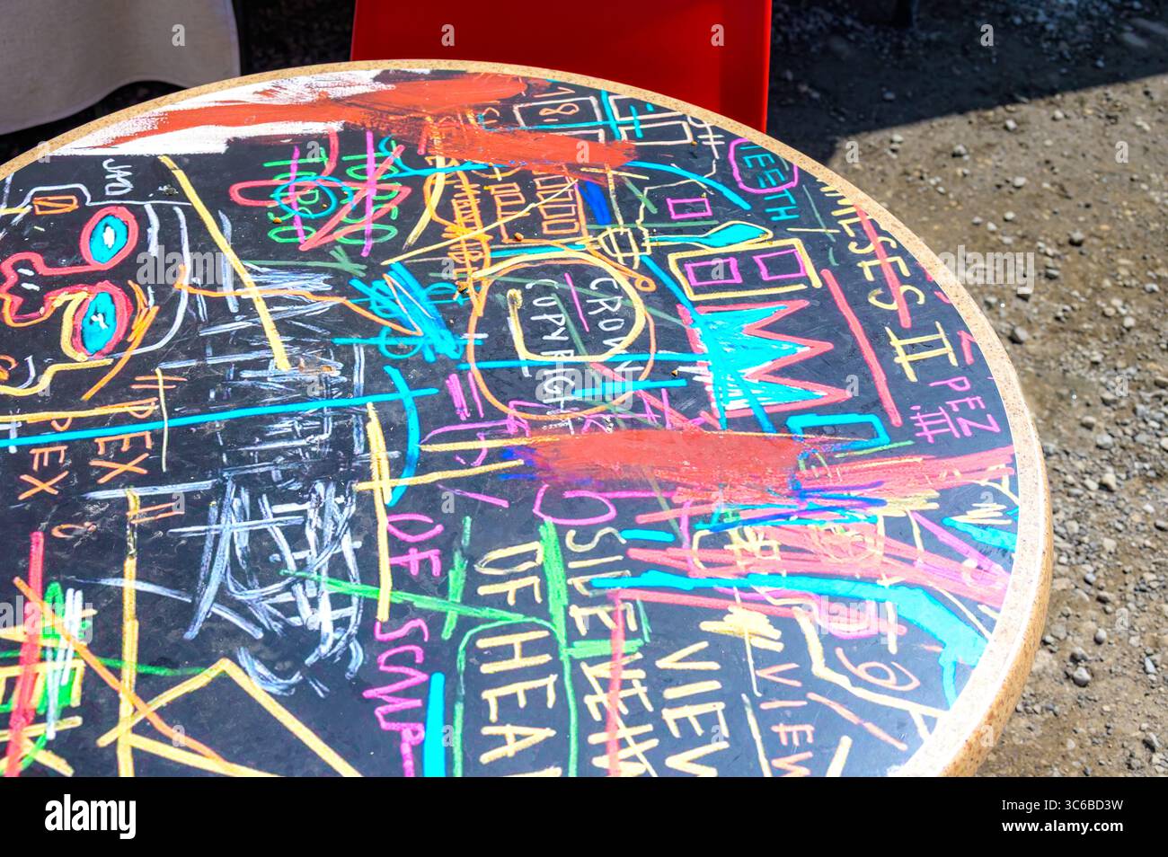 Eine runde Tischplatte ist mit Graffiti aus Neonkreide, farbenfrohem Text und abstrakten Zeichnungen bedeckt, die von Street Art und Pop-Symbolik inspiriert sind. Stockfoto