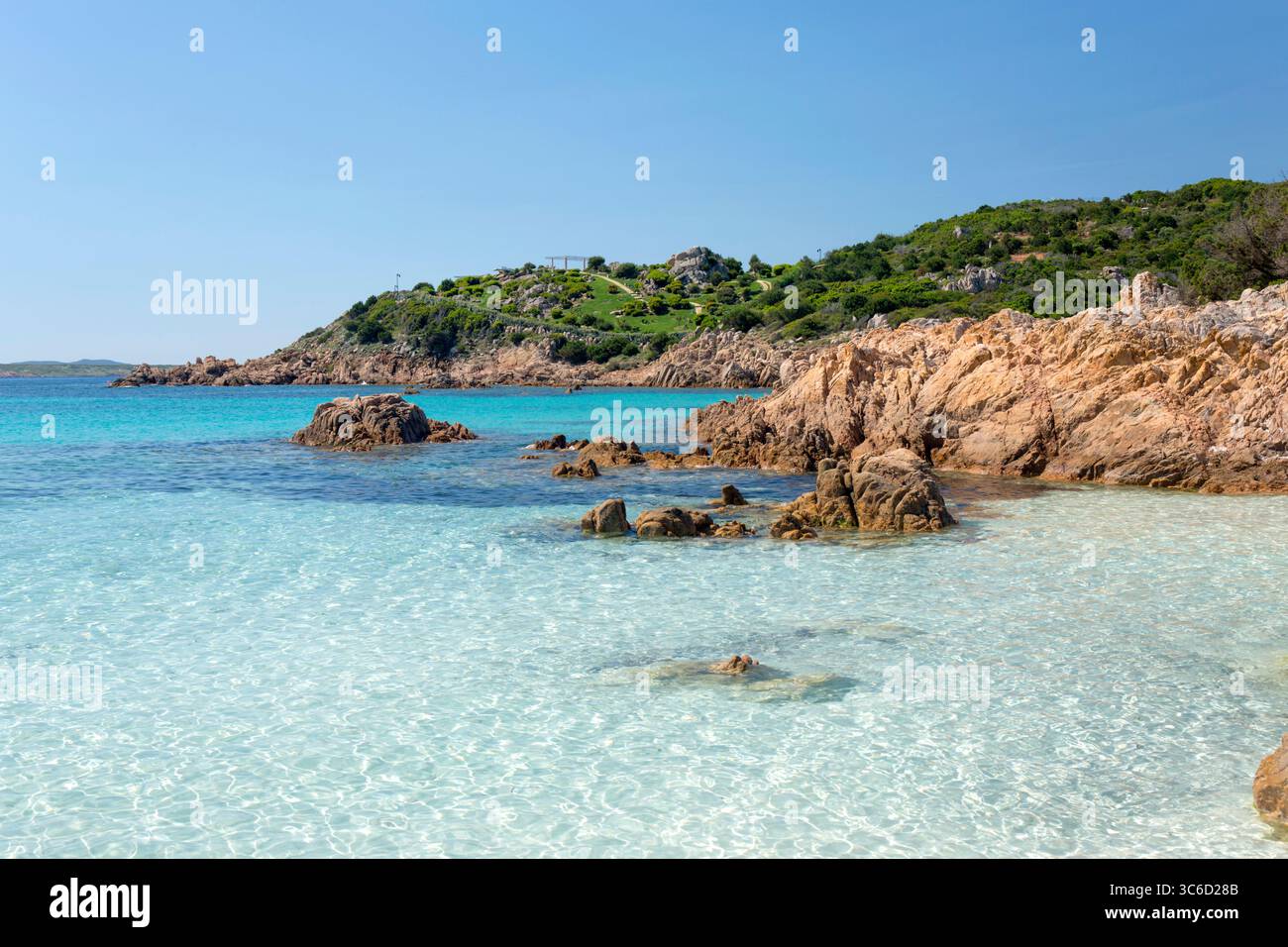 Romazzino, Costa Smeralda, Gallura, Sardinien, Italien. Blick von der Spiaggia del Principe über klares Flachwasser zur bewaldeten felsigen Halbinsel. Stockfoto