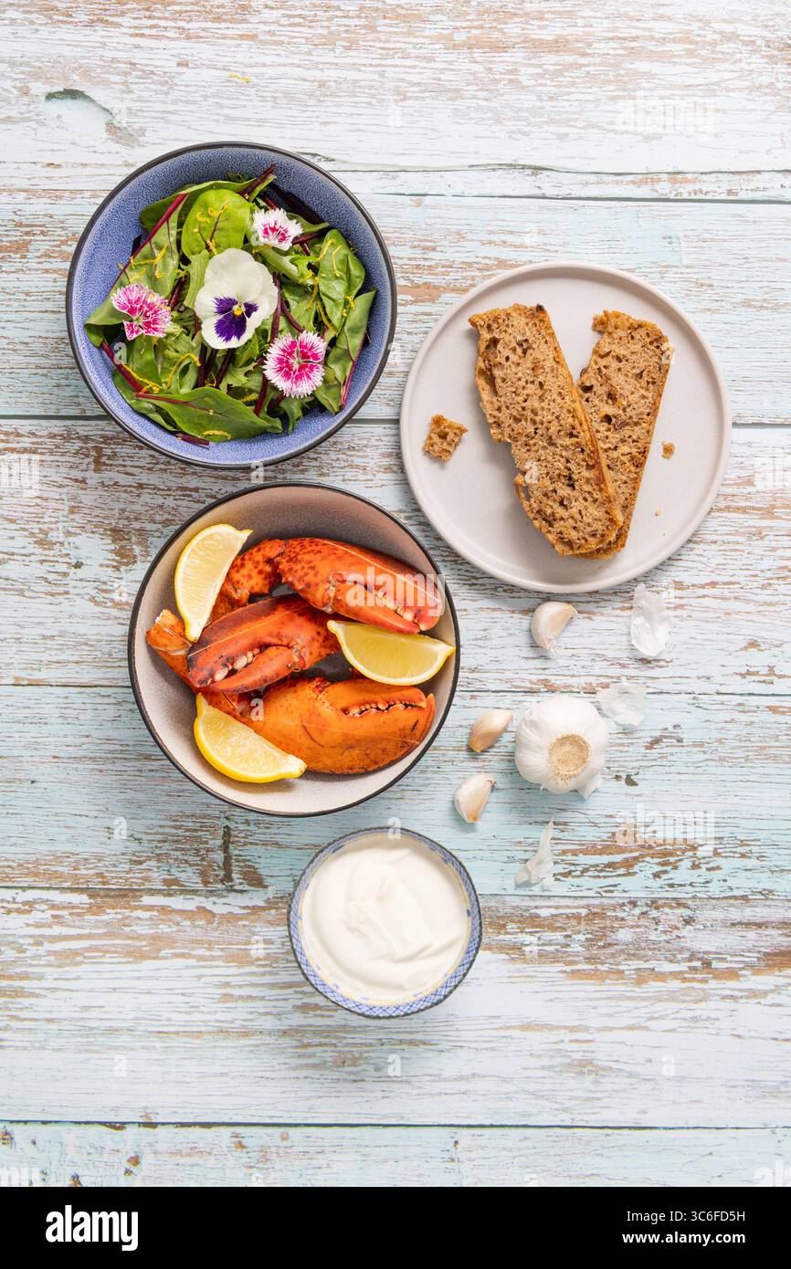 Studio-Aufnahme von Hummer-Klauen aus Farmfood, serviert mit hausgemachtem Sauerteig, grünem Salat und essbaren Blumen aus dem Garten. 🏷️ Schlüsselwörter (Rechte M Stockfoto