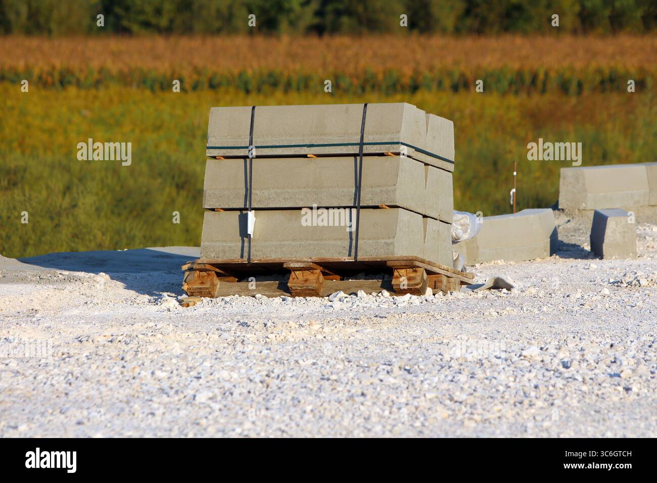 Ein Bündel rechteckiger, mit schwarzen Bändern gebundener Betonfertigteile befindet sich auf einer Holzpalette, die von Kies umgeben ist, an einer Straßenbaustelle Stockfoto