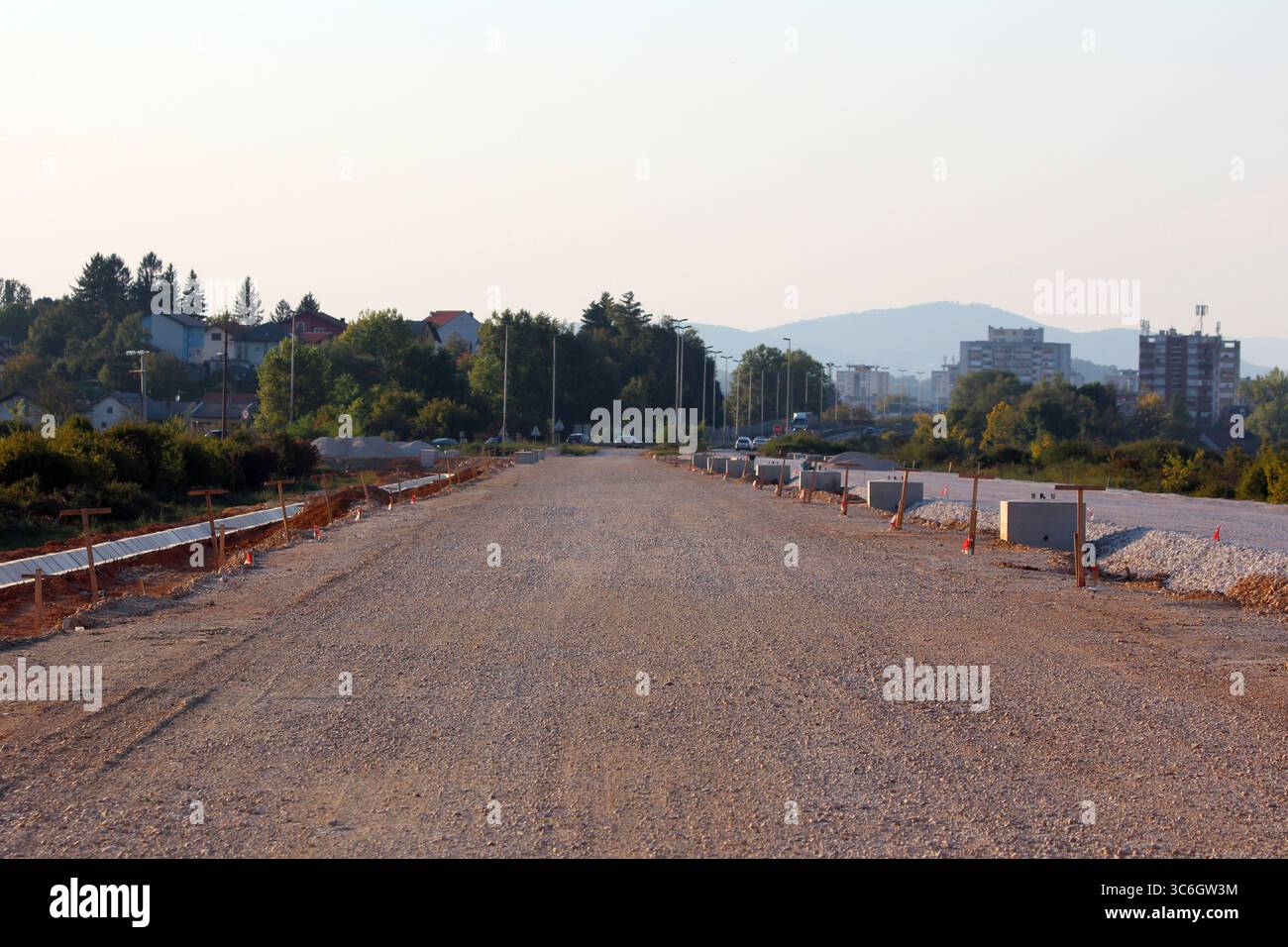 Ein langer Abschnitt von unbefestigtem Straßenfundament mit platzierten und noch zu installierenden Bordsteinen säumt beide Seiten und zeigt eine aktive Tiefbautechnik Stockfoto