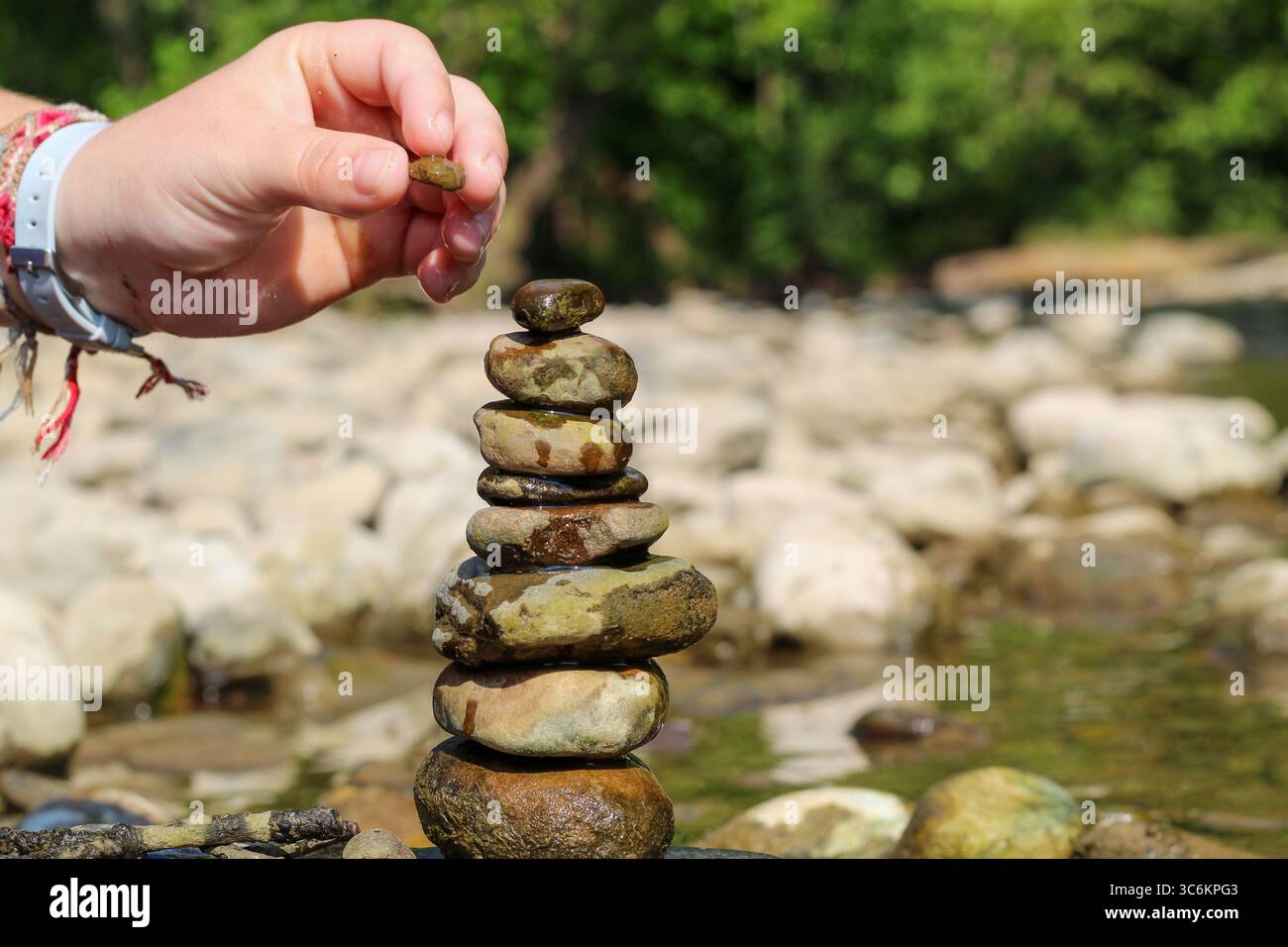 Nahaufnahme der Hände, die Felsen an einem Fluss in einer friedlichen natürlichen Umgebung stapeln Stockfoto