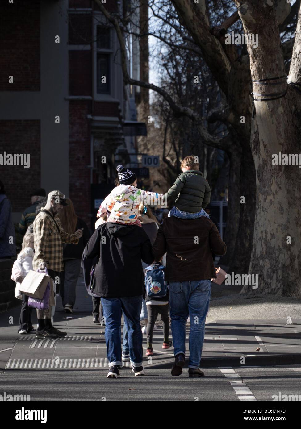 2 Kinder, die die Hände auf der Schulter der Eltern halten, die Straße überqueren, melbourne Stockfoto