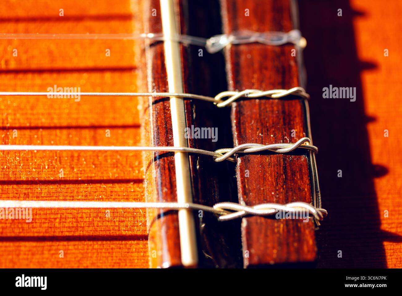 Holzbrücke mit Nylonsaiten an Akustikgitarre. Klassische Gitarre mit Nylonsaiten mit Naturholzoberfläche. Nahaufnahme hebt die zarte Stk Stockfoto