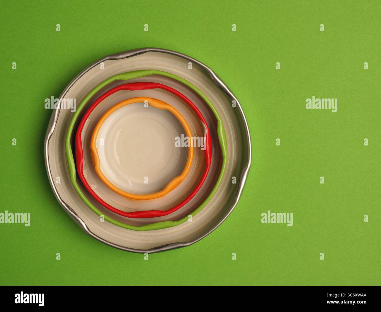 Bunte Weißblechdeckel auf grünem Hintergrund mit Textraum, Ansicht von oben, Recyclingkonzept Stockfoto