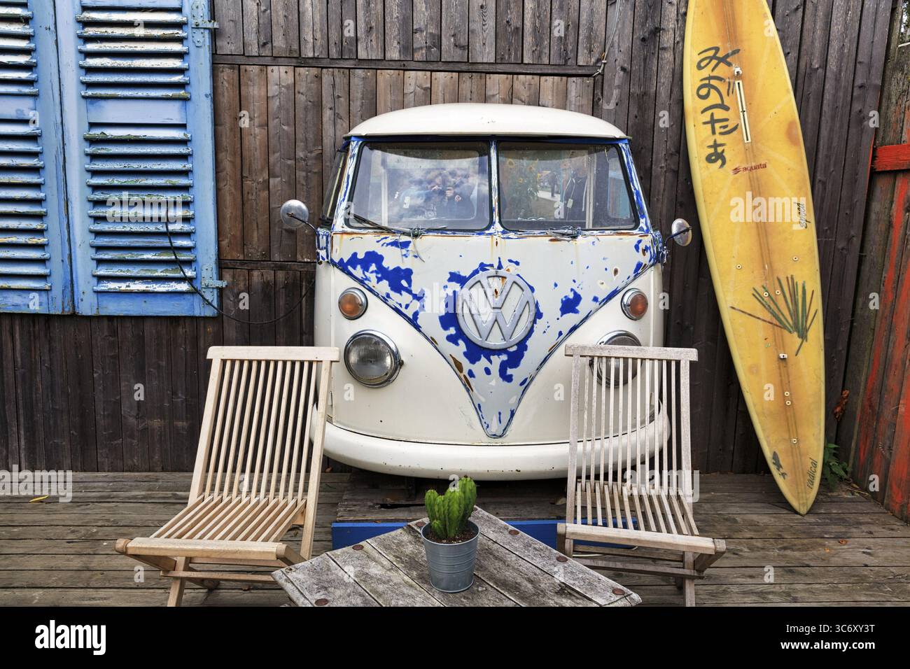 Ursprüngliche Terrasse, Vorderseite VW Bus T1, Bulli, Oldtimer, Holzfassade mit Surfbrett als Dekoration, Tisch und Holzstühle, Café, Strandbar, Huede Stockfoto