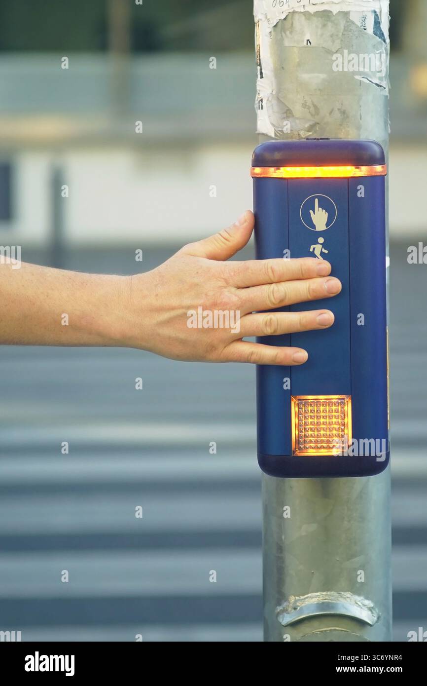 Fußgänger drückt die Taste an der Stadtüberquerung, um die Ampel, vertikales Foto, zu aktivieren. Smart City: Barrierefreiheit zur Förderung der urbanen Mobilität Stockfoto