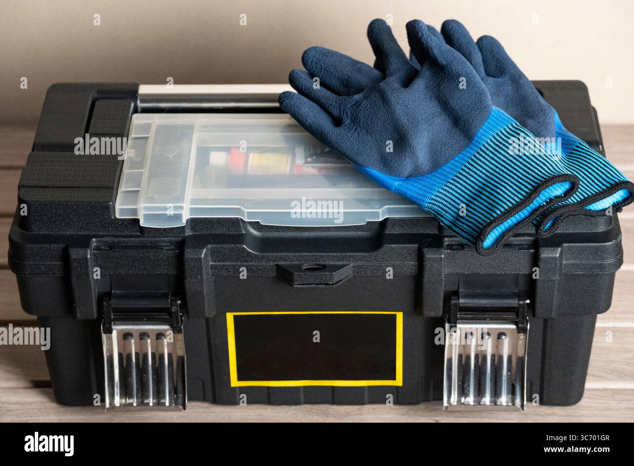 Blaue Schutzhandschuhe auf einem schwarzen Kunststoff-Werkzeugkasten mit transparenten Fächern. Ideales Image für den Bau und die Verbesserung von Häusern Stockfoto