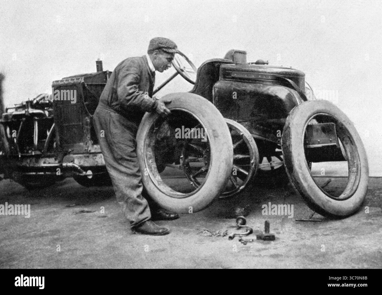 Der erste Grand Prix des ACF (1906) wurde durch das erstmalige Erscheinungsbild des abnehmbaren Rads gekennzeichnet. Dieses Bild zeigt Szisz, der einen Reifen seines Renault wechselt Stockfoto