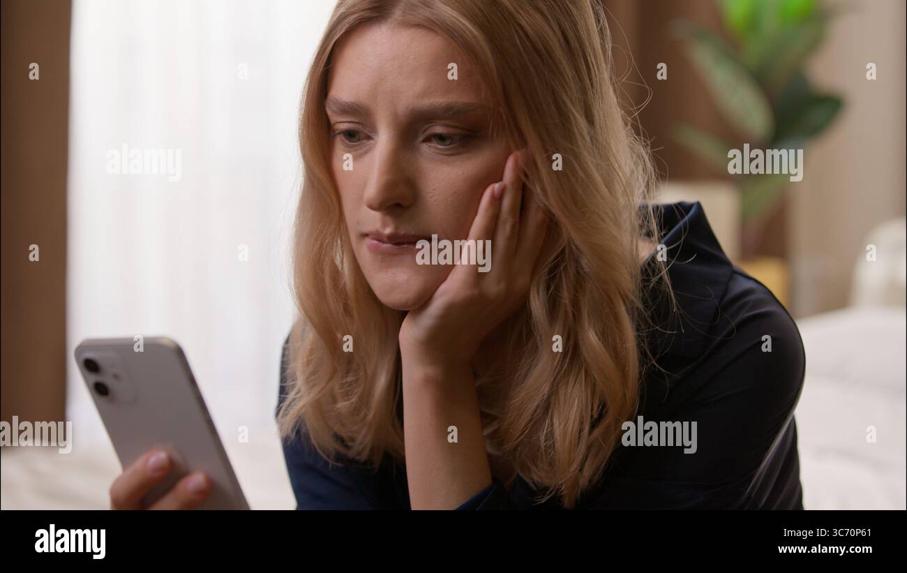 Ängstlich enttäuscht kaukasische Frau liest negative Nachrichten Handy Bankrott im Schlafzimmer Frau hält Smartphone Dame fühlt sich besorgt frustriert Stockfoto