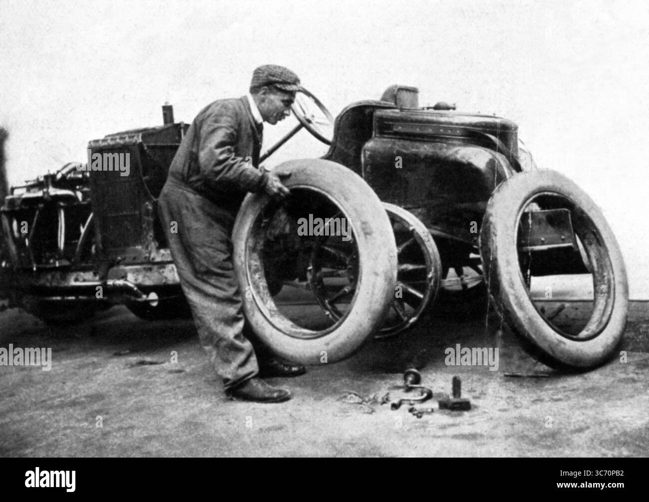 Der erste Grand Prix des ACF (1906) wurde durch das erstmalige Erscheinungsbild des abnehmbaren Rads gekennzeichnet. Dieses Bild zeigt Szisz, der einen Reifen seines Renault wechselt Stockfoto