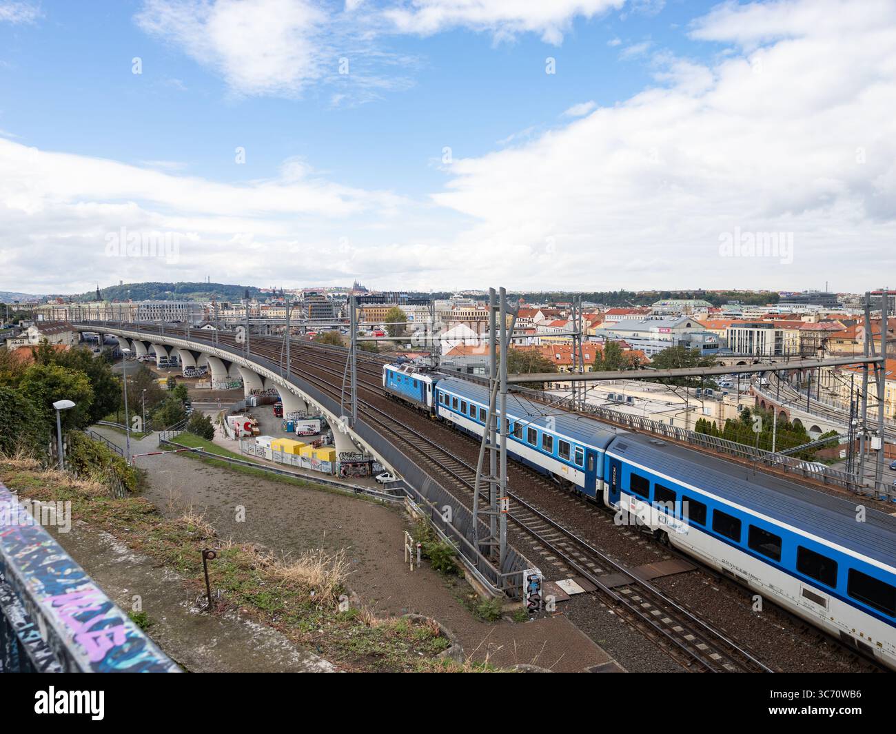 Zug der České dráhy (Tschechische Eisenbahnen) auf der Bahnstrecke in Prag. Großes Brückengebäude in der Hauptstadt. Öffentliche Verkehrsmittel in Tschechien. Stockfoto