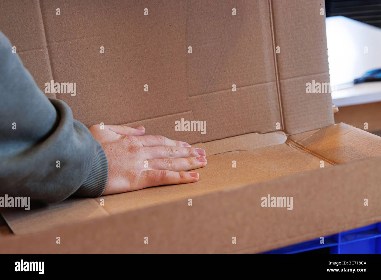 Person, die den Rand einer Pappschachtel faltet, zur Wiederverwendung oder zum Recycling fest drückt und die Kartonverpackung für die Entsorgung vorbereitet. Stockfoto