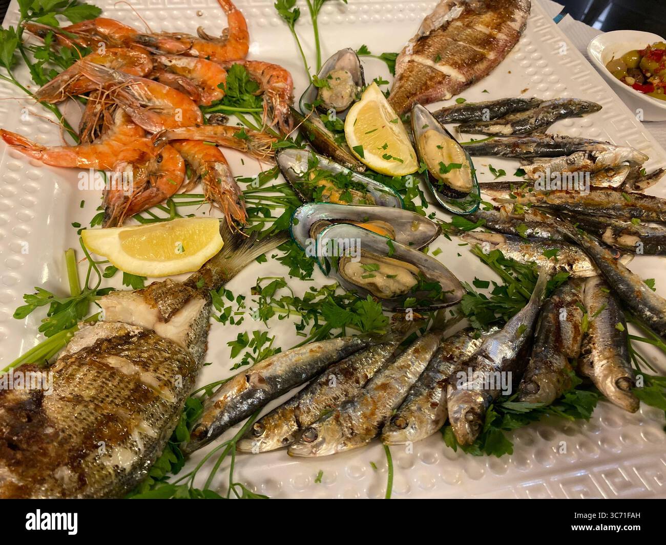 Eine köstliche Meeresfrüchte-Platte mit gegrilltem Fisch, Garnelen und Muscheln auf einem weißen Teller. Stockfoto