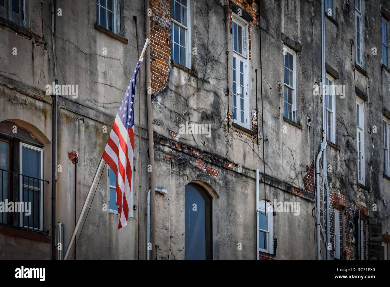 Die Sonne erwärmt eine amerikanische Flagge auf einem verwitterten Gebäude in Savannah, Georgia. Stockfoto