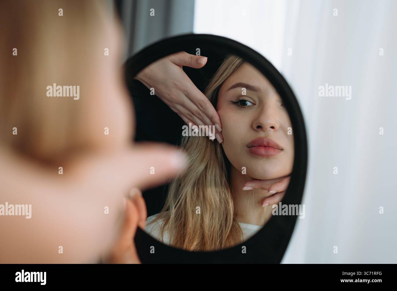 Junge Frau, die in einen Spiegel schaut nach Faziumverjüngungsverfahren in der ästhetischen Klinik Stockfoto
