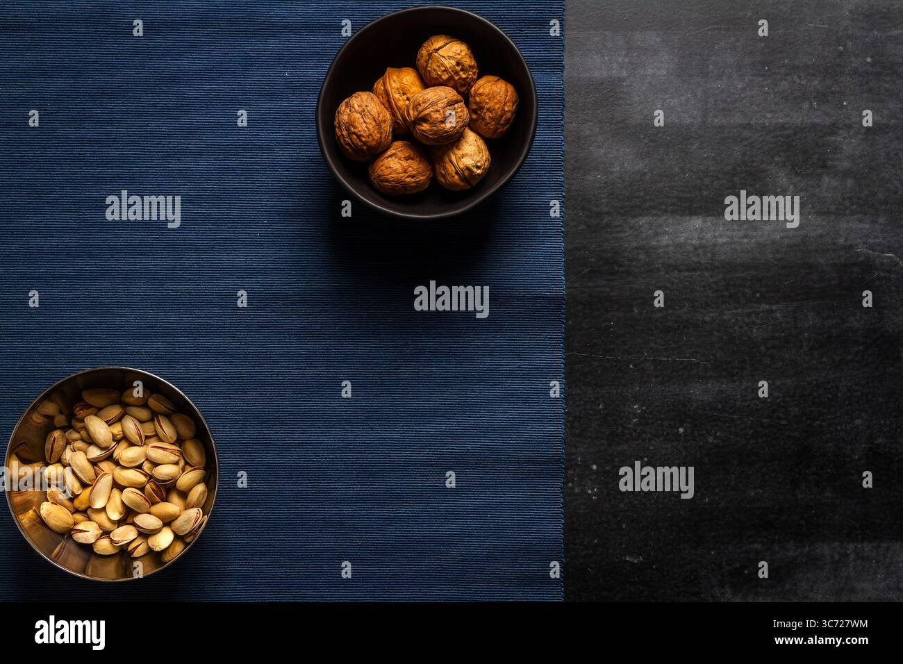Schwarze Schüssel mit Walnüssen und blauem Tischtuch auf schwarzem Tafel Hintergrund. Flache Lagen. Draufsicht. Stockfoto