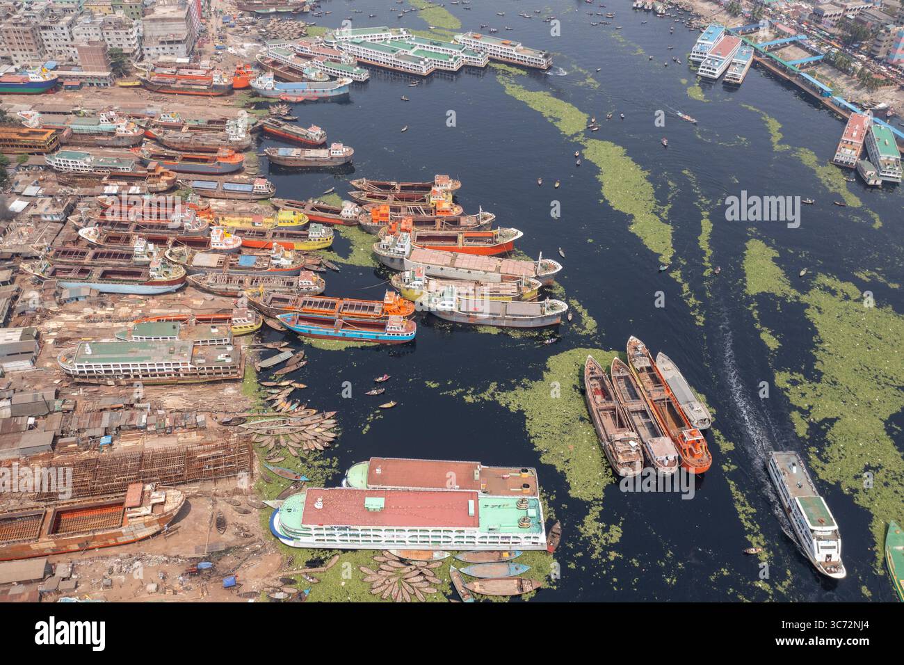 Aus der Vogelperspektive auf eine Wasserstraße voller Fähren und Boote, die den Himmel reflektiert, umgeben von den Gebäuden, Keraniganj, Dhaka Division, Bangladesch. Stockfoto