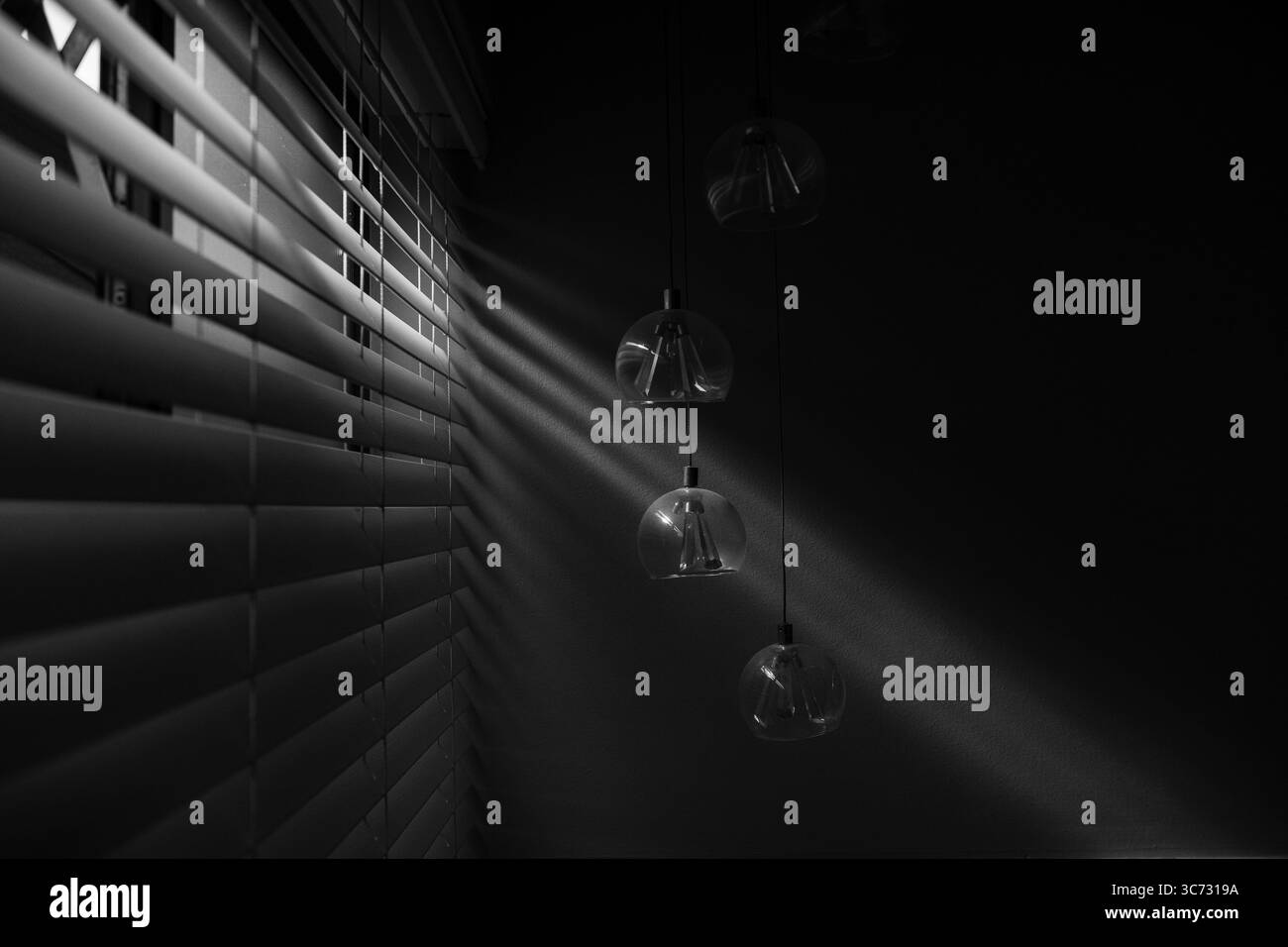 Jalousien im venezianischen Stil leicht offen, mit einer eng einstrahlenden, eleganten Glasleuchte Stockfoto