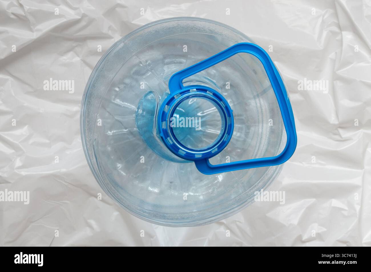 5-Liter-Kunststoffflasche mit blauem Griff oben auf weißem Polyethylen-Hintergrund, Draufsicht Stockfoto