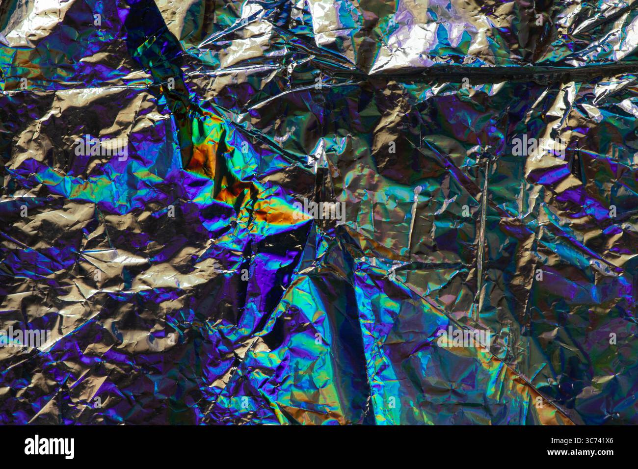 Holographische Folie mit zerknittertem Regenbogen und leuchtendem Glanz in violetten, blauen, grünen und goldenen Farben, abstraktem Hintergrund oder Designvorlage Stockfoto