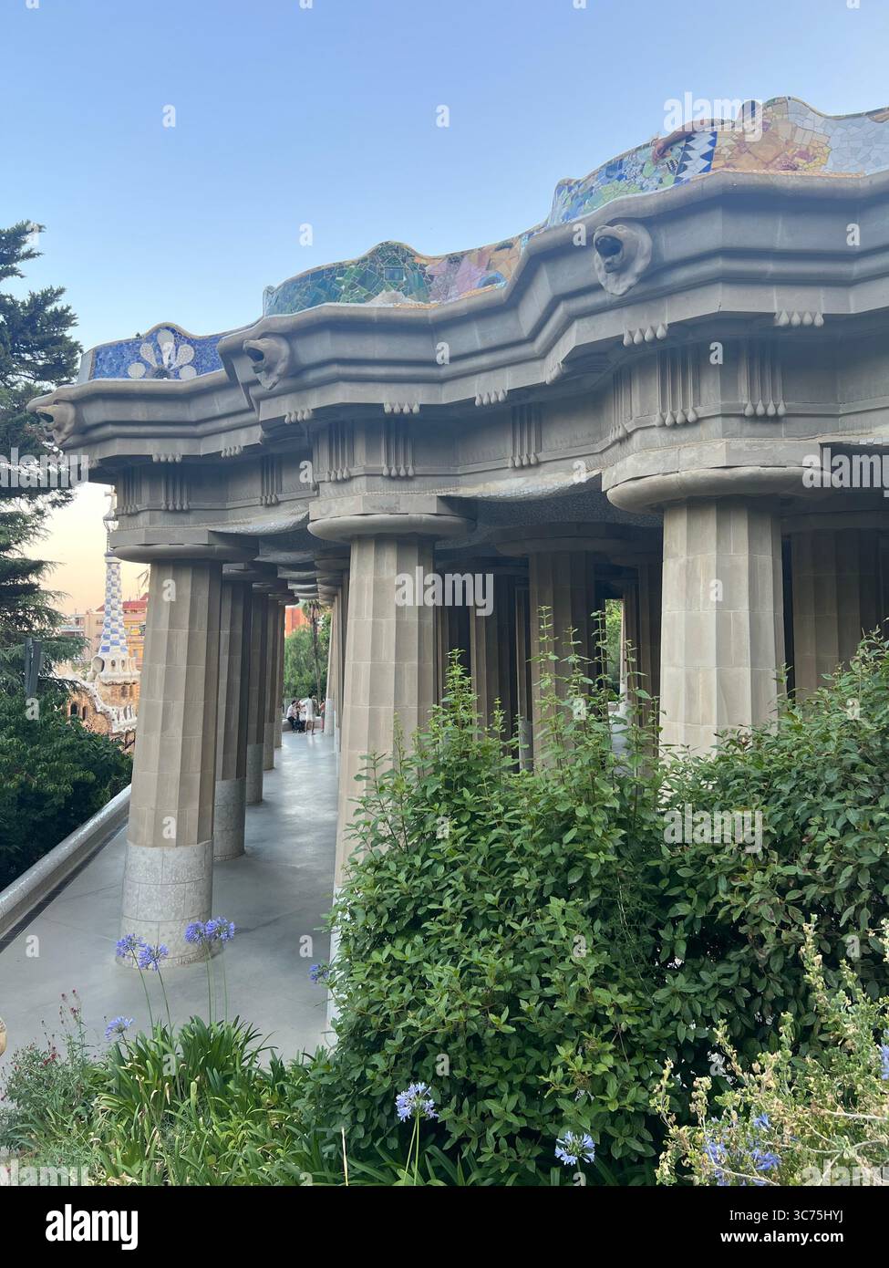 Blick auf die Hypostyle Halle vom hinteren Eingang des Park Güell, mit den dorischen Säulen von Gaudí und dem ikonischen Mosaikbalkon darüber, Barcelona, Katalonien Stockfoto
