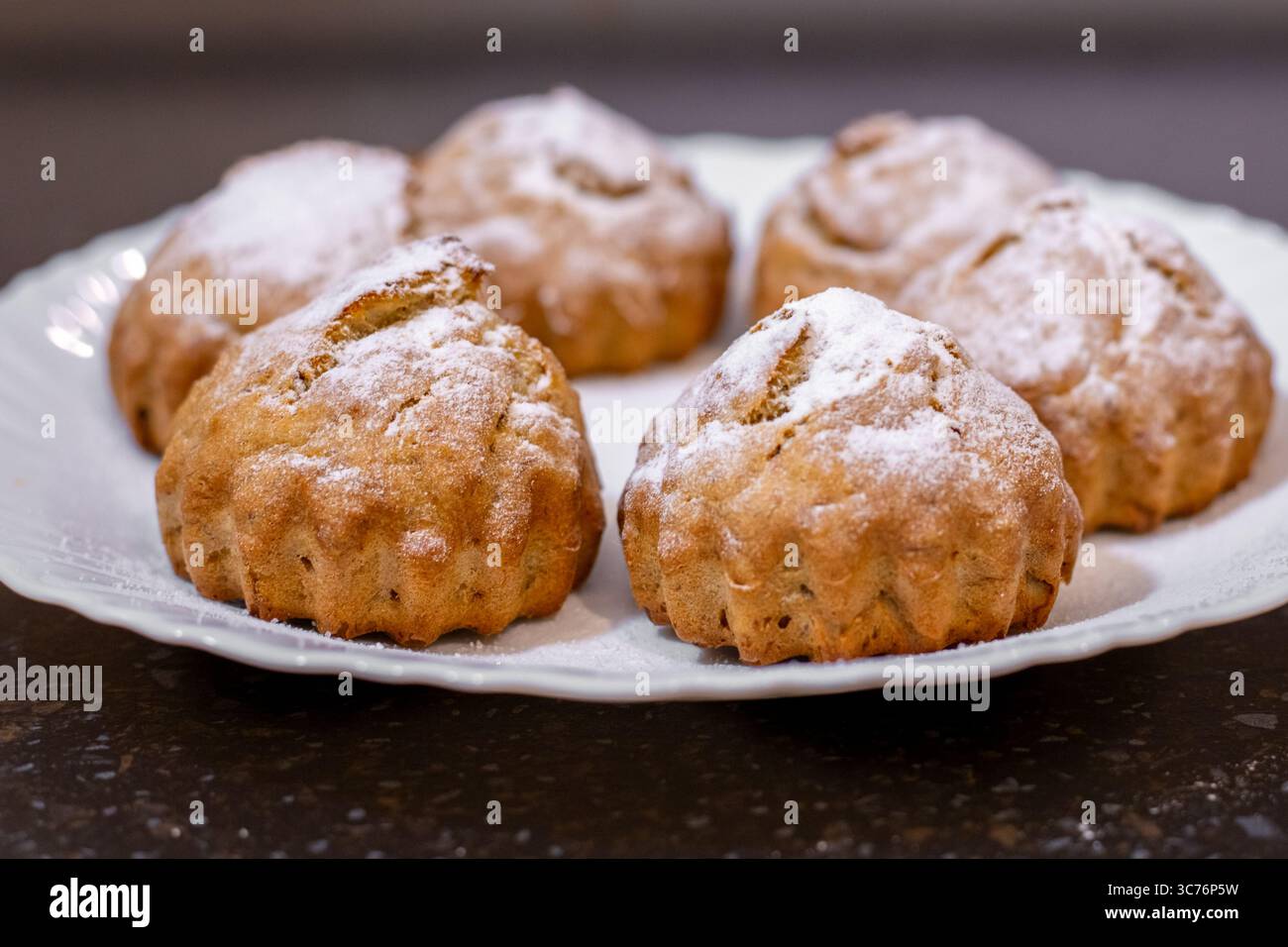 Frisch gebackene Bananenmuffins elegant auf einem weißen Teller angeordnet, mit Puderzucker bestäubt. Stockfoto