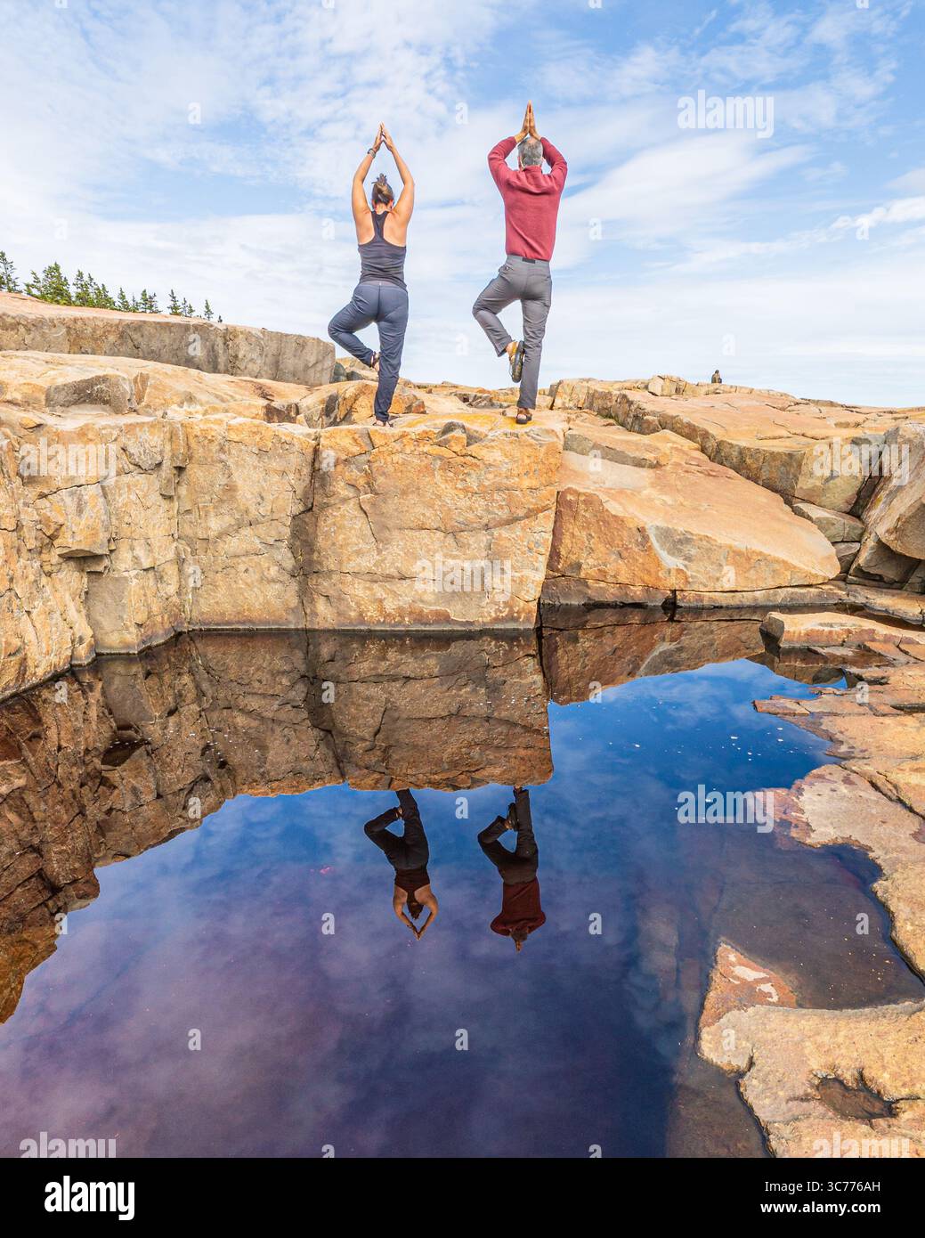 Reflected Cliffside Yoga Bliss fängt einen ruhigen Moment im Acadia-Nationalpark ein, wo zwei Individuen auf dem felsigen Gelände das Gleichgewicht finden. Die Ruhe Stockfoto