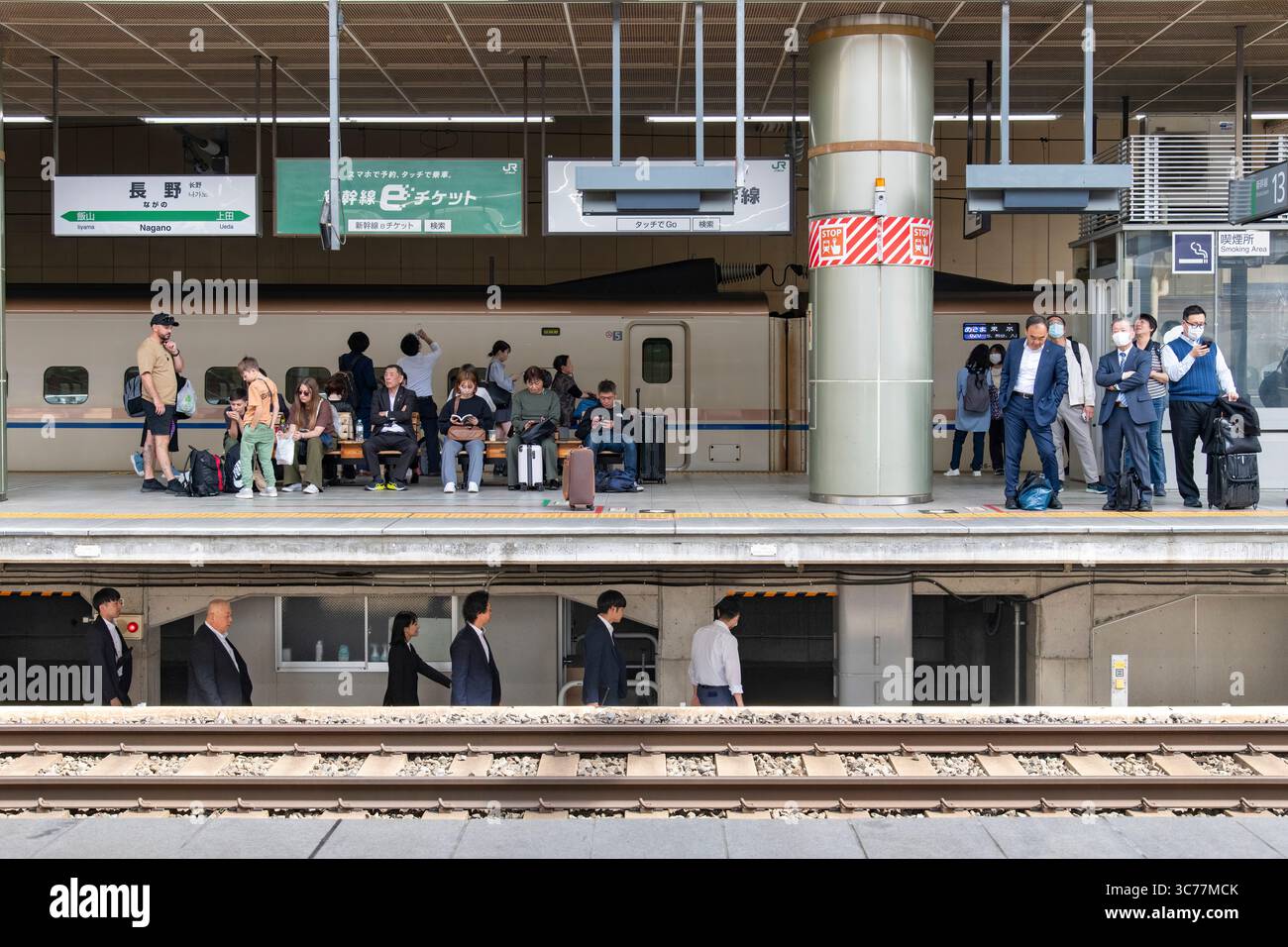 Nagano, Japan - 22. April 2025: Der Bahnsteig am Bahnhof Nagano ist mit wartenden Fahrgästen beschäftigt, während das Eisenbahnpersonal durch die Passage unter der Pl Stockfoto