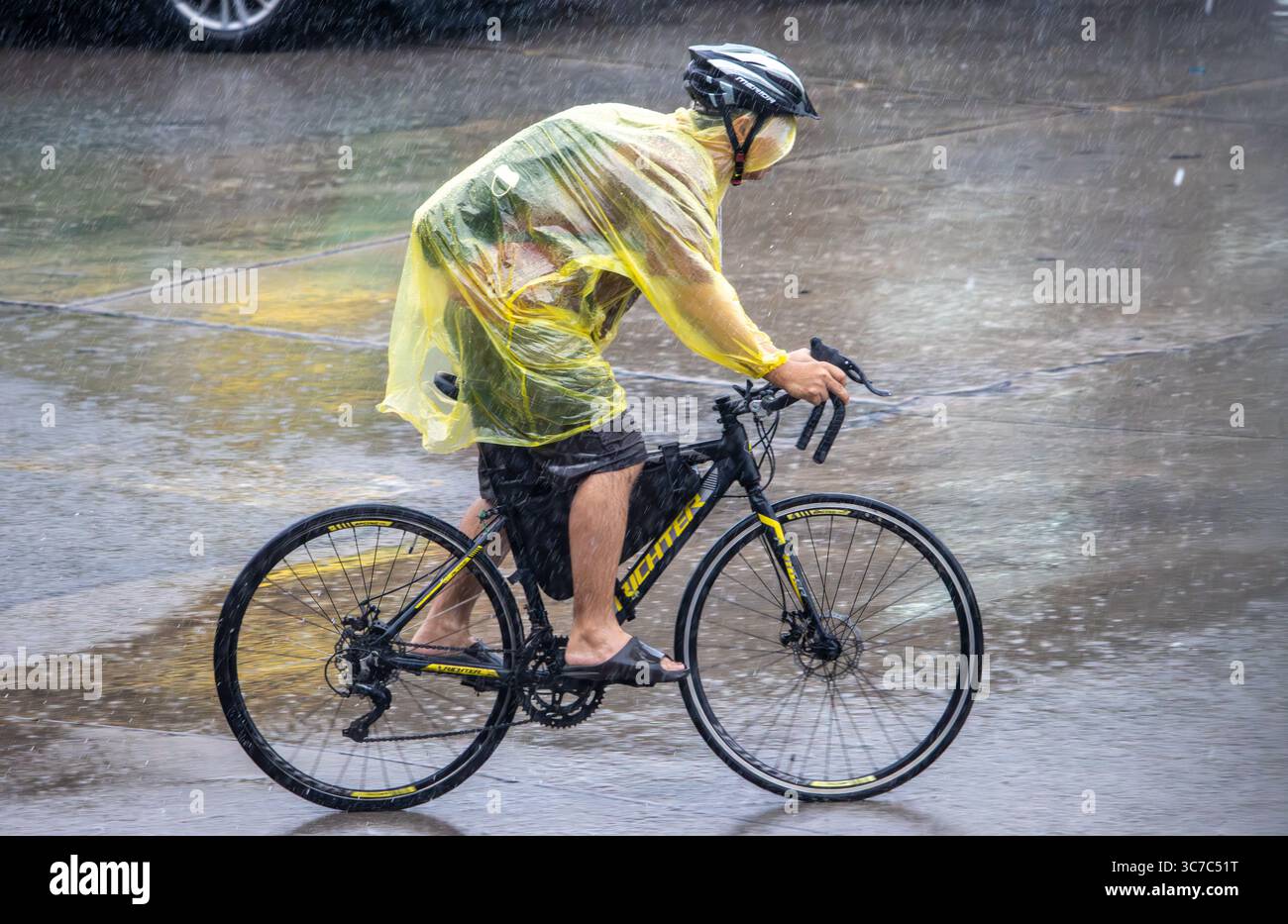 SAMUT PRAKAN, THAILAND, 27. JUNI 2025, Radfahrer im Regenmantel reitet durch starken Regen auf einer Stadtstraße Stockfoto
