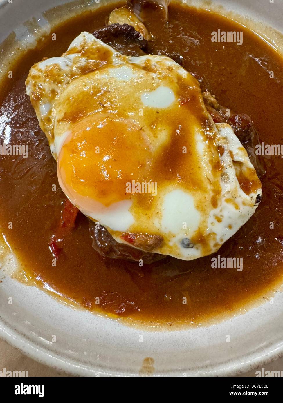 Traditionelles portugiesisches Gericht mit Steak und Spiegelei, serviert in einer kräftigen braunen Sauce. - Smartphone-aufgenommenes Stockfoto