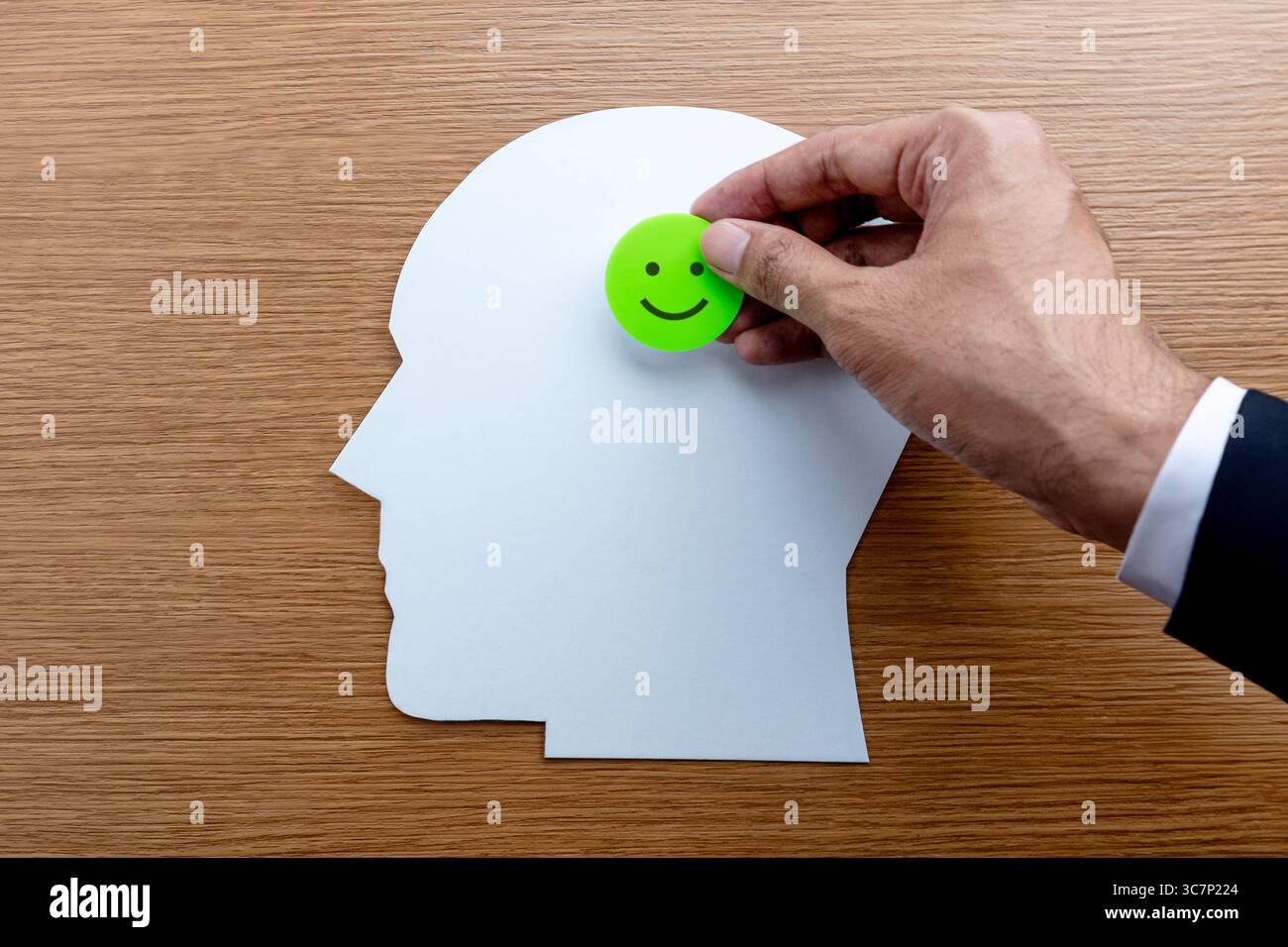 Eine Hand, die einen kleinen grünen Kreis mit einem glücklichen Gesicht auf den Ausschnitt des menschlichen Kopfes legt. Geistige Gesundheit, positives Denken, glückliches Gedankenkonzept. Stockfoto