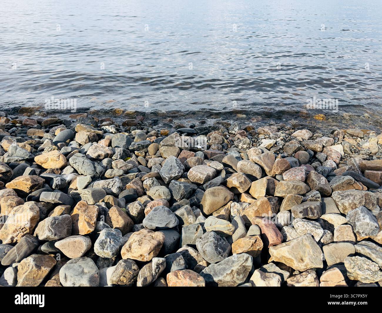Das Seeufer ist mit Felsen bedeckt, während das Wasser sanft gegen sie schlägt. Stockfoto