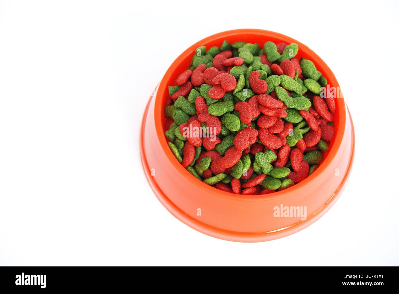 Rote und grüne Katzenkibble in der orangefarbenen Schüssel auf weißem Hintergrund Stockfoto